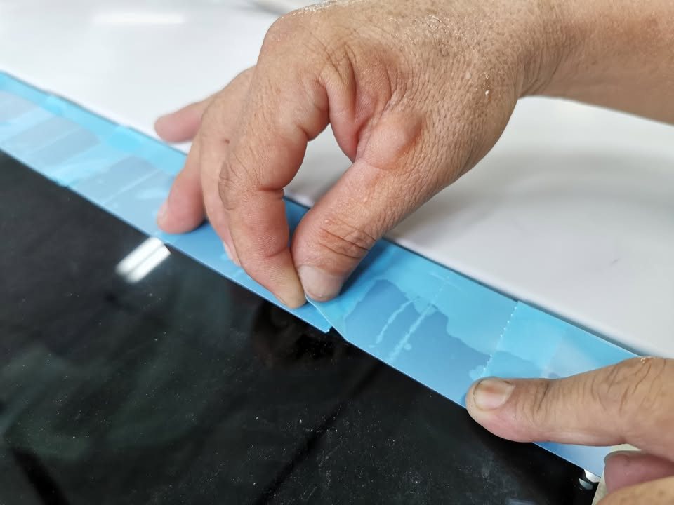 Blue masking tape being laid along the edge of the glass.