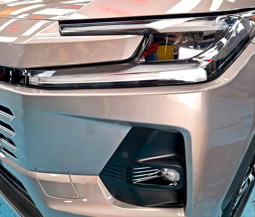 Close-up of the RAV4 headlight and front bumper with workshop lights reflected in the paint.