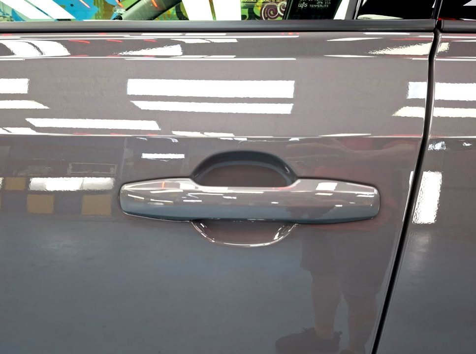 Door handle on the grey RAV4 with workshop lights reflected in the panel.