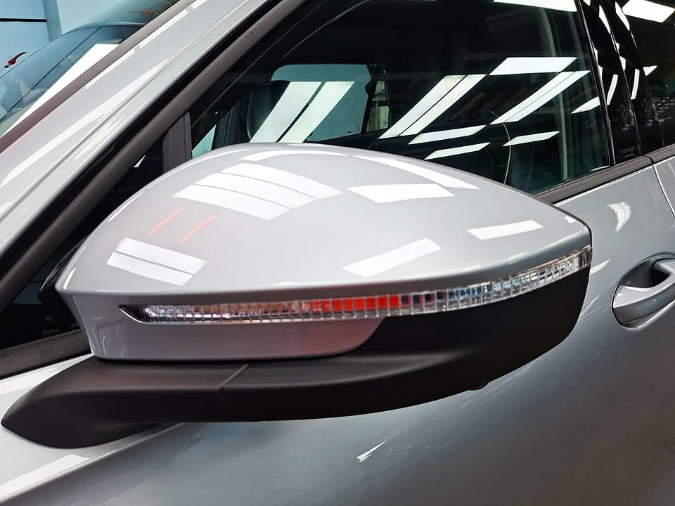 Body-coloured wing mirror with indicator strip, reflecting the workshop lights.