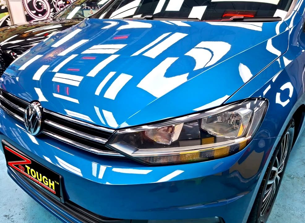 Front of the blue Touran with ceiling lights reflected across the bonnet.