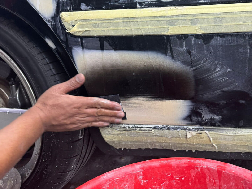 A technician wet-sanding a panel on the Volvo S60R, working the surface level.