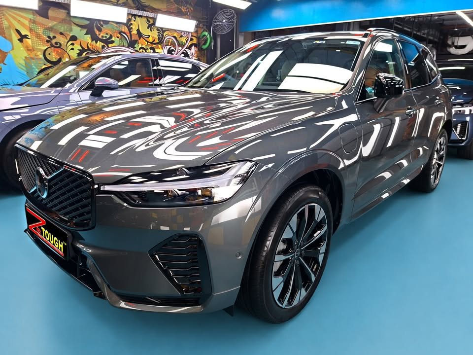 Grey Volvo XC60, front three-quarter view in the workshop, with ceiling lights reflected across the bonnet and a ZeTough plate on the front.