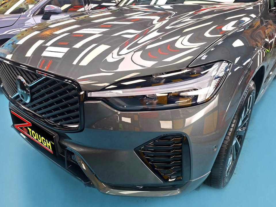 Front of the XC60 showing the grille and headlight, with sharp reflections in the bonnet.