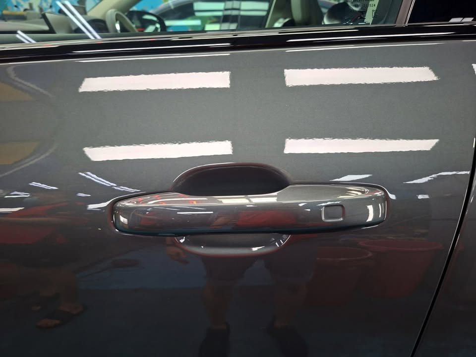 Door handle on the grey door panel with ceiling lights reflected in the paint.