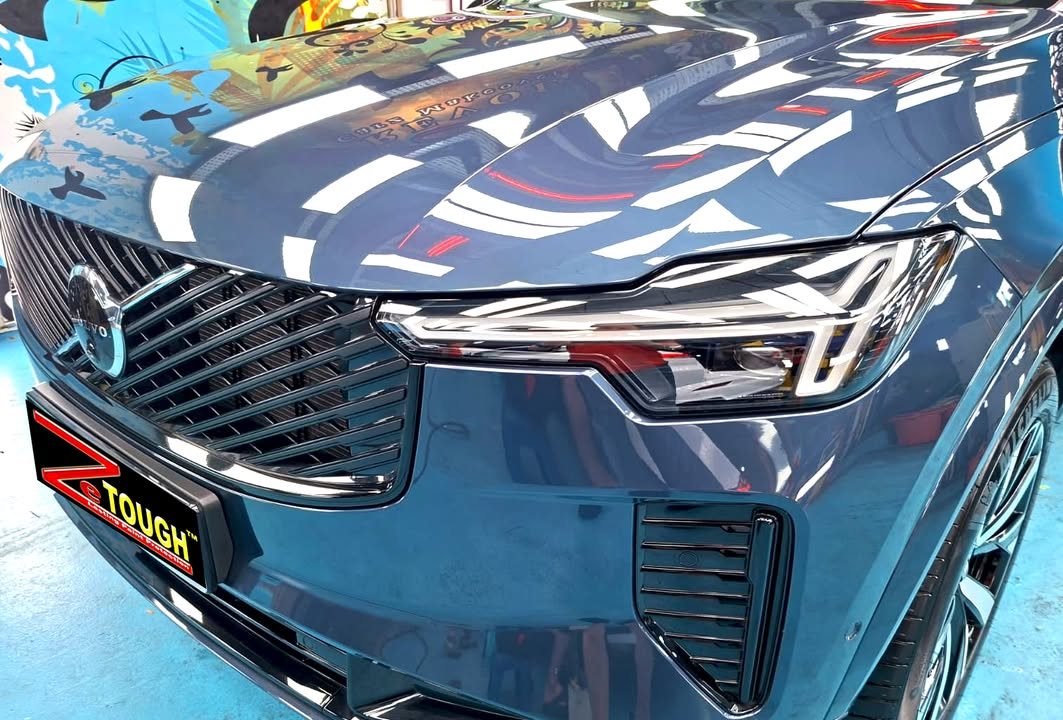 Grille and headlight of the blue XC90 with reflections on the bonnet.