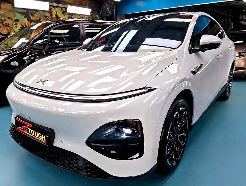 White Xpeng G6, front three-quarter view in the workshop with a ZeTough plate on the bumper.