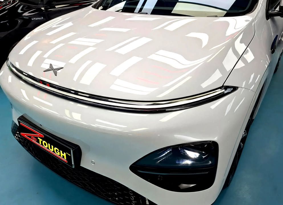 Front of the white Xpeng G6 showing the light bar and bonnet reflections.