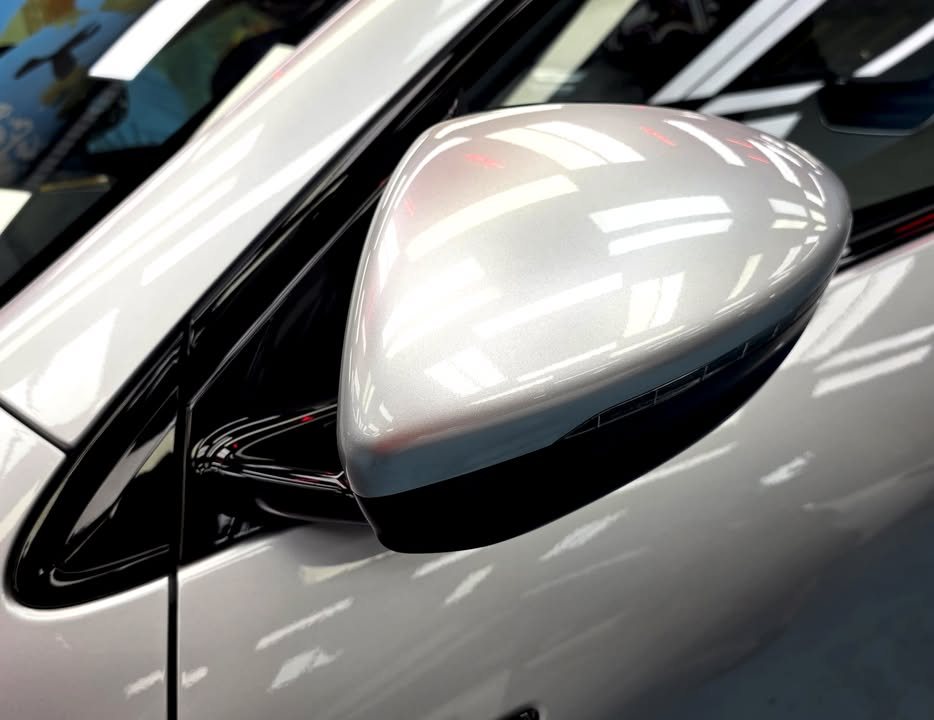 Silver side mirror of the Xpeng G6 reflecting the workshop lights.