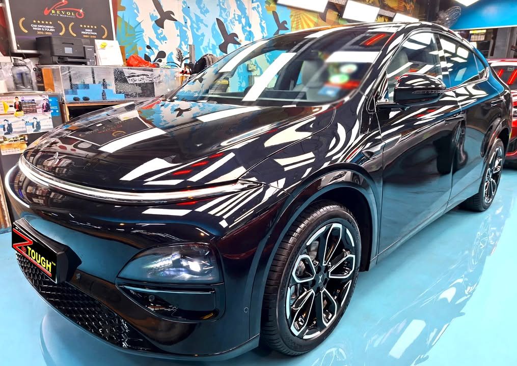Black XPeng G6, front three-quarter view in the workshop, with ceiling lights reflected across the bonnet and a ZeTough plate on the front.