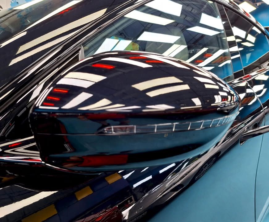 Black side mirror cap reflecting the workshop ceiling lights.