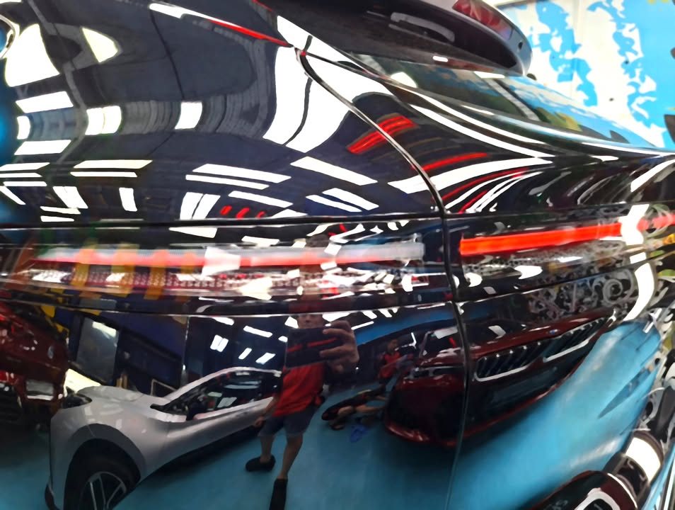 Rear quarter panel and tail light with workshop lights reflected in the black paint.