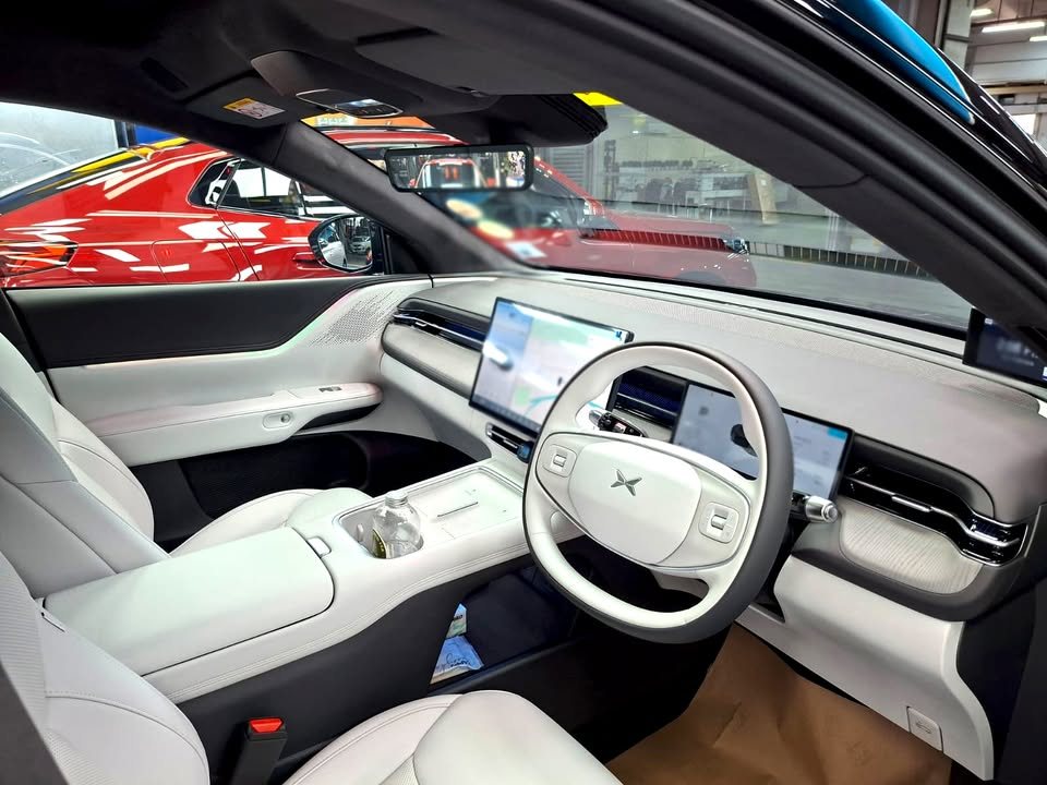 Cabin with light grey seats, white steering wheel and wide dashboard screens.