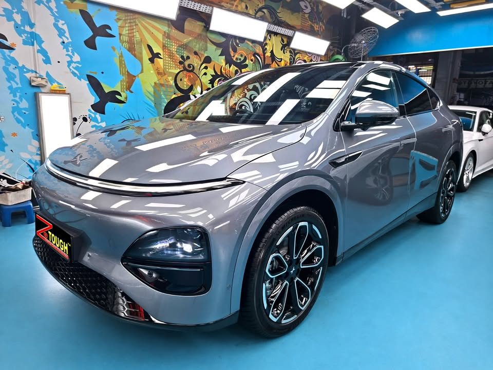 Grey Xpeng G6 from the front three-quarter in the Revol workshop, with a ZeTough plate on the bumper.