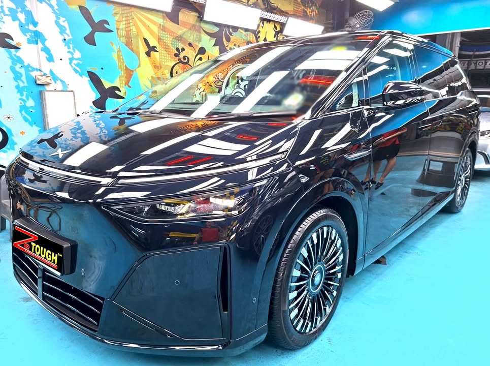 Front three-quarter view of a dark XPeng X9 in the Revol Carz hall with lights reflected along the body.