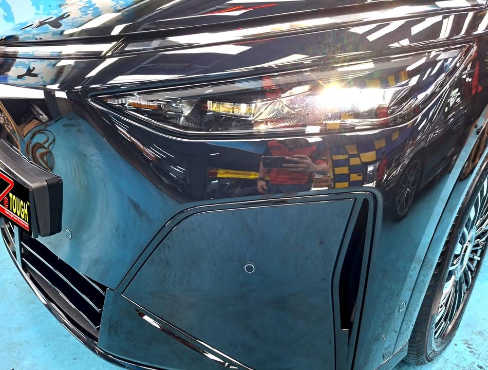 Close-up of the X9 headlight and front bumper in glossy dark paint.