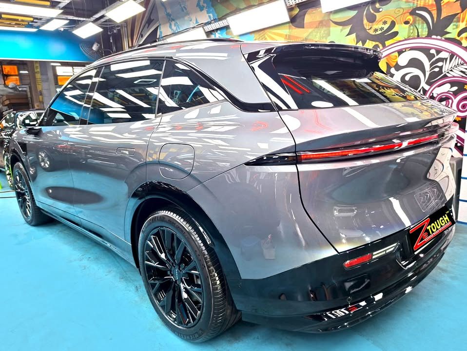 Rear three-quarter view of the grey Zeekr 7X showing the full-width tail light and black wheels.