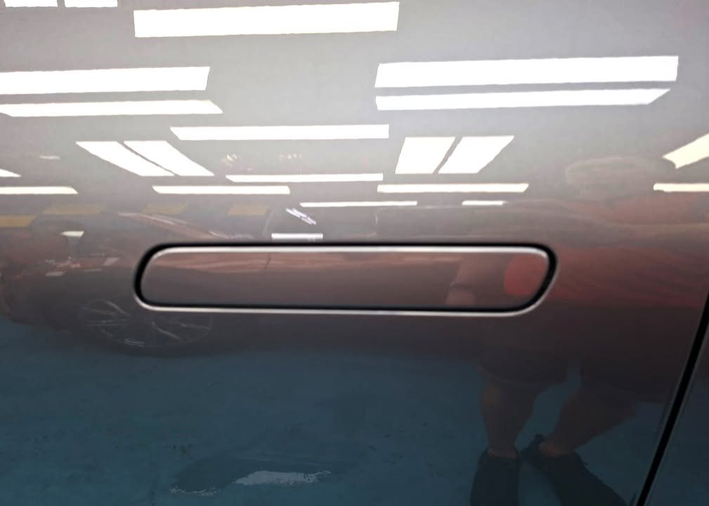 Flush door handle on a grey panel with light reflections.
