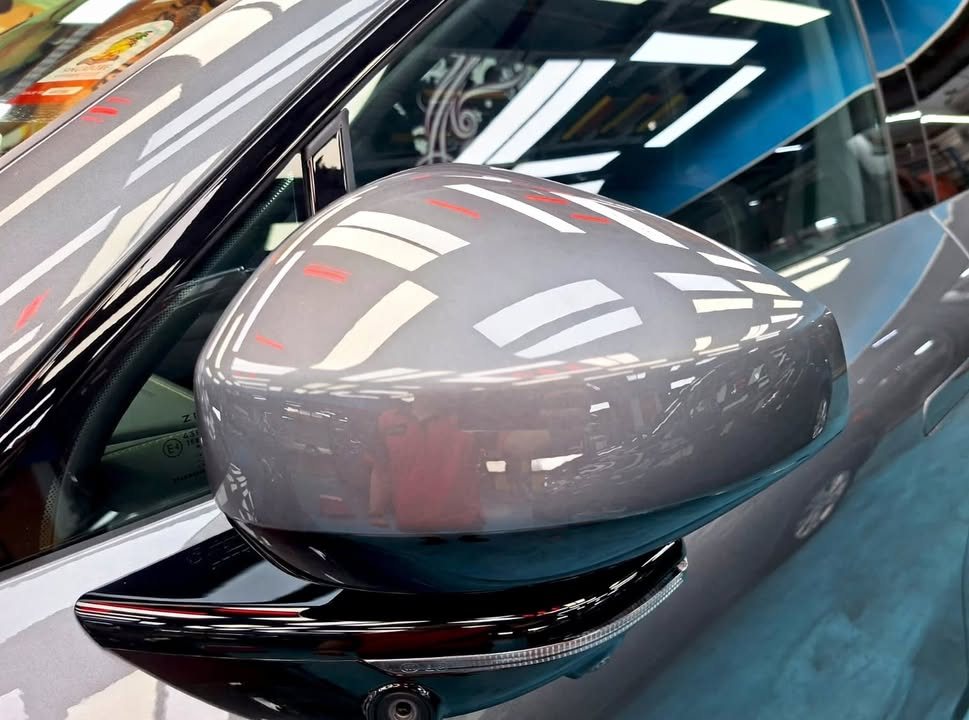 Close-up of the grey side mirror cap reflecting the workshop ceiling lights.