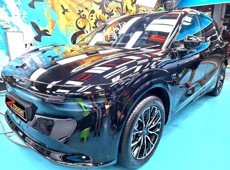 Black Zeekr 7X from the front three-quarter, its bonnet and wings reflecting the workshop lights after the ZeTough Titanium coating.