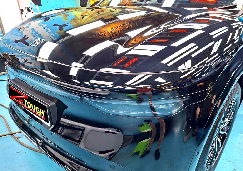 Front of the black Zeekr 7X with the light strip and bonnet reflecting overhead lights.